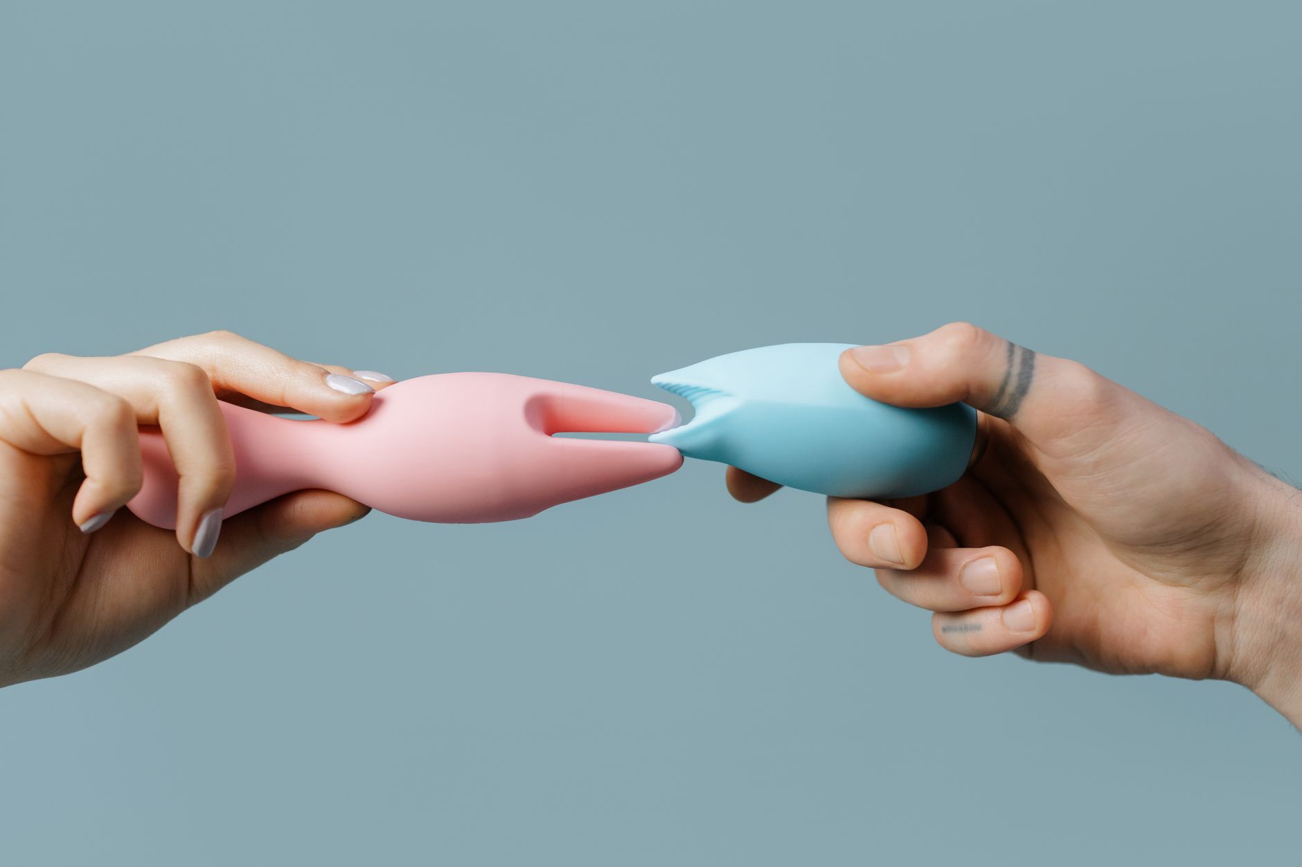 Hands holding silicone clitoral vibrators in different colors against a neutral background