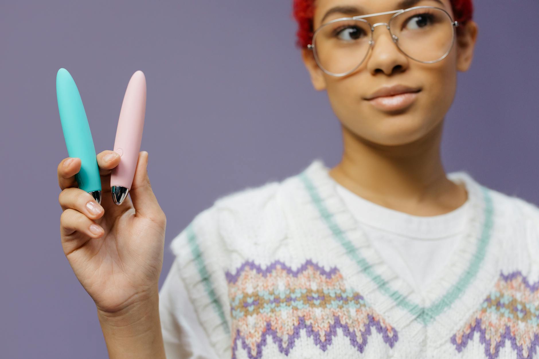 Intimate close-up of hands holding a sleek blue vibrator against a purple background