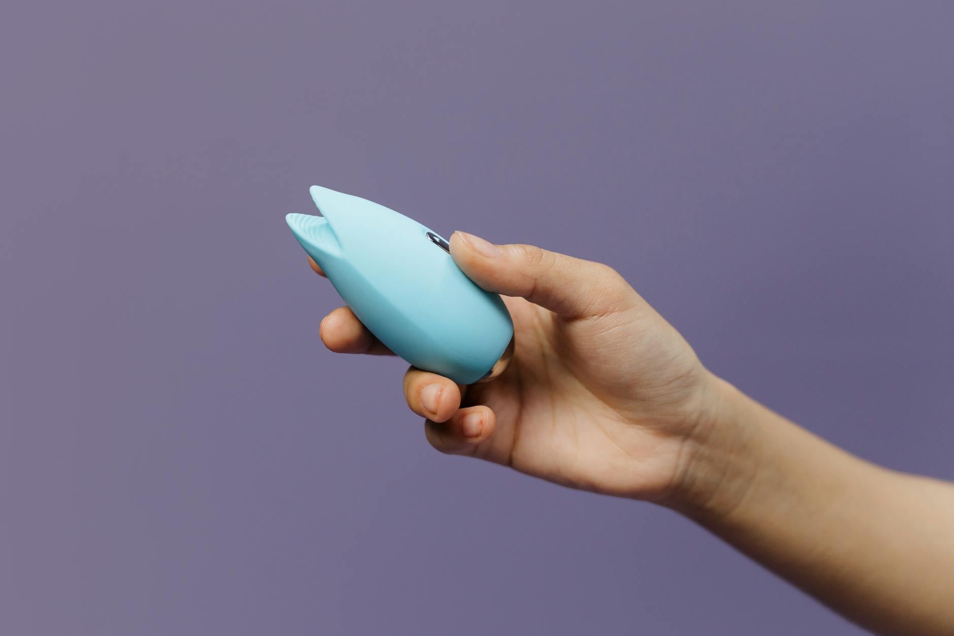 Blue clitoral vibrator held in hand against purple background, representing accessible pleasure tools for anxiety